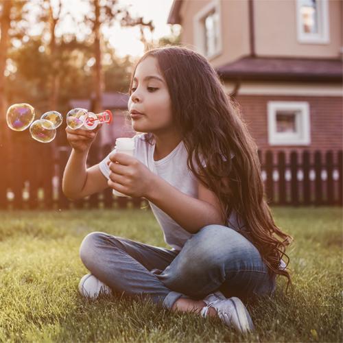 Mädchen sitzt im Garten und macht Seifenblasen